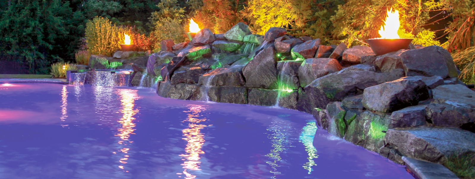Rock waterfall and fire bowls at night on Exton swimming pool.