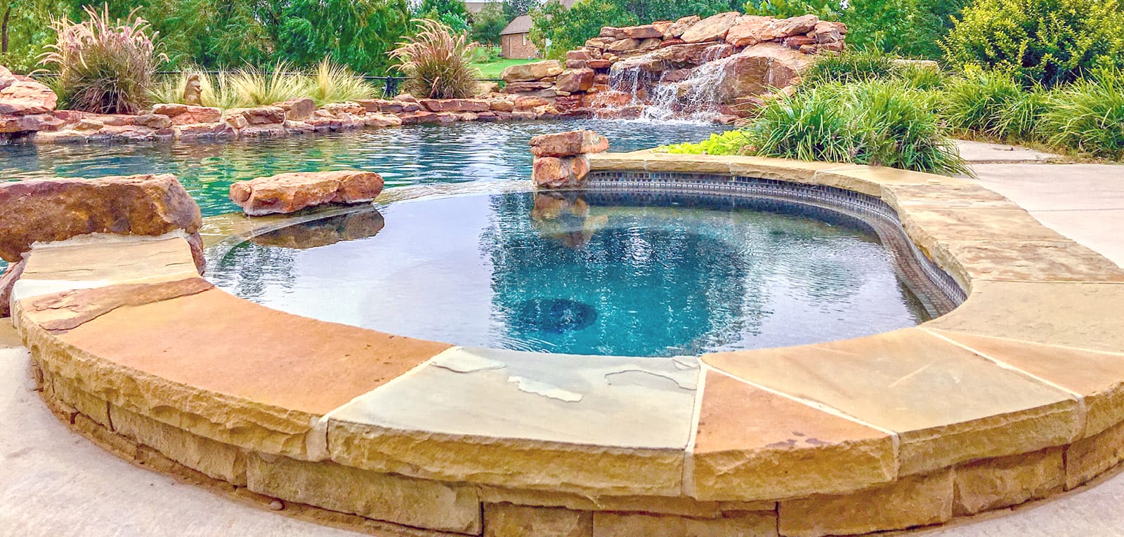 Organic-shaped spa on a swimming pool with a rock waterfall.