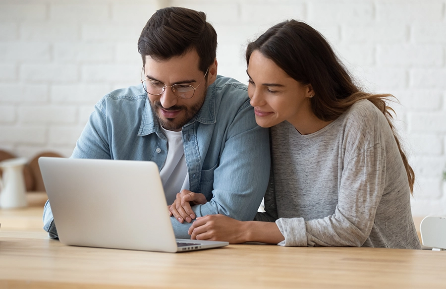 Husband and wife sitting together looking at a laptop computer at home.