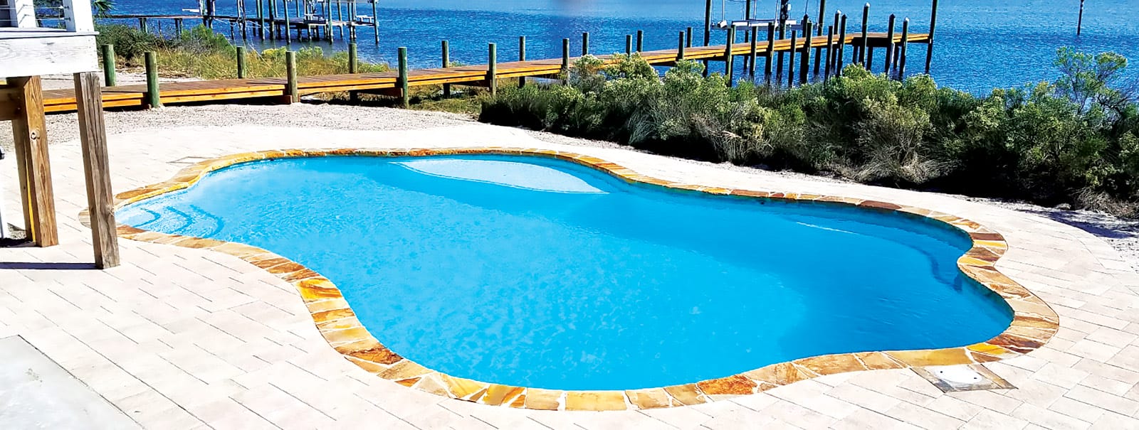 Inground pool with flagstone-trimmed perimeter by dock on ocean. 