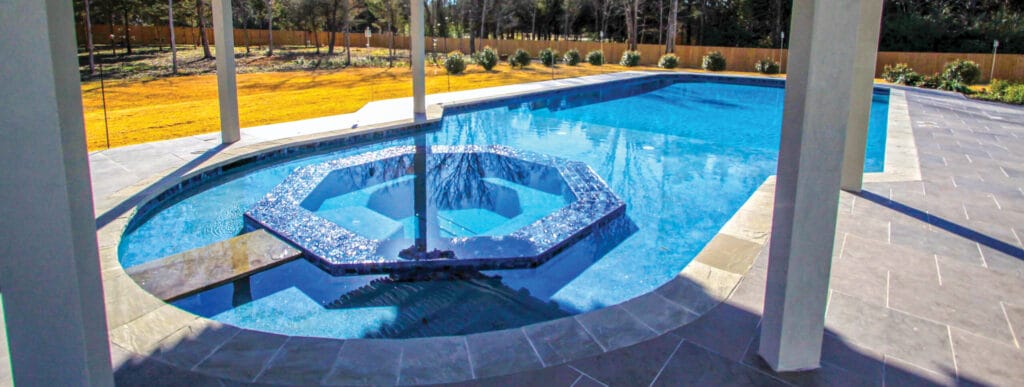 Hexagon-shaped spa with stone bridge on backyard swimming pool.