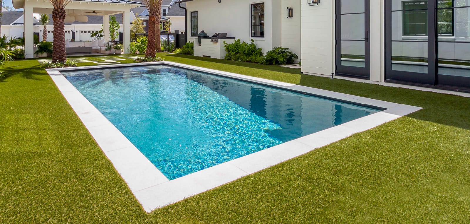 Rectangle custom pool surrounded by grass lawn in a backyard.