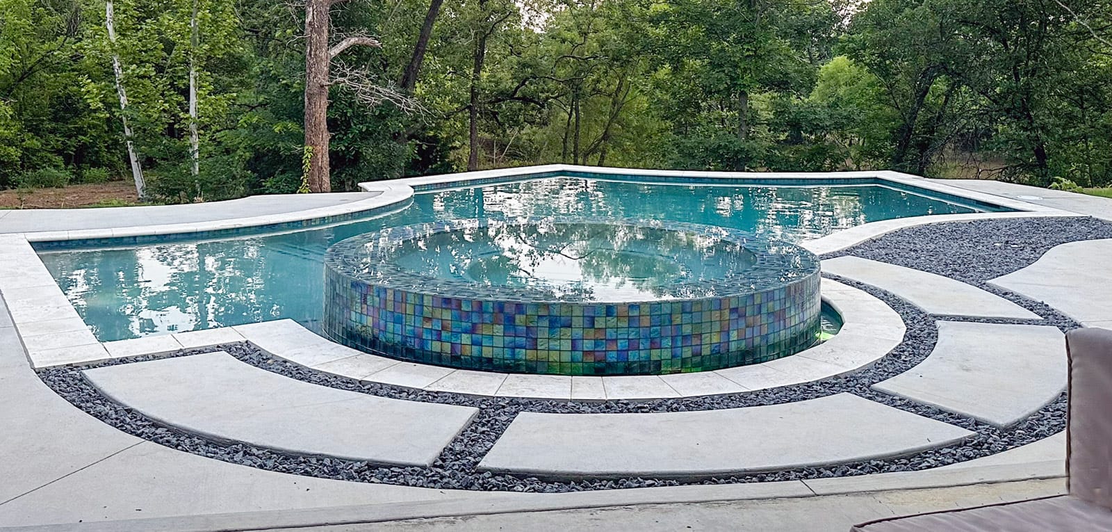 Geometric-shaped custom pool with elevated rimflow spa covered in iridescent tile.