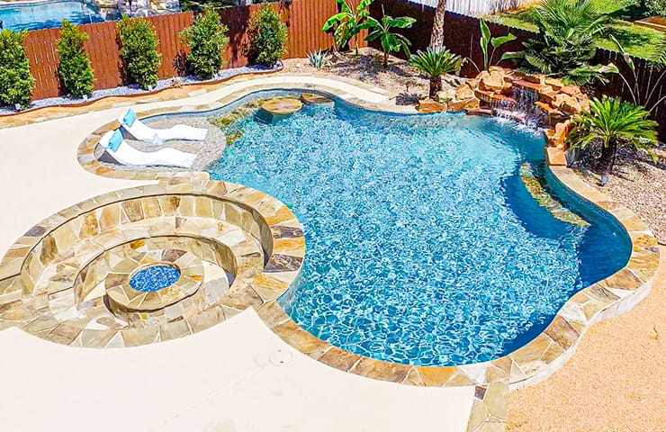 lagoon style inground pool with tanning ledge, swim-up table, rock waterfall, and a large fire pit