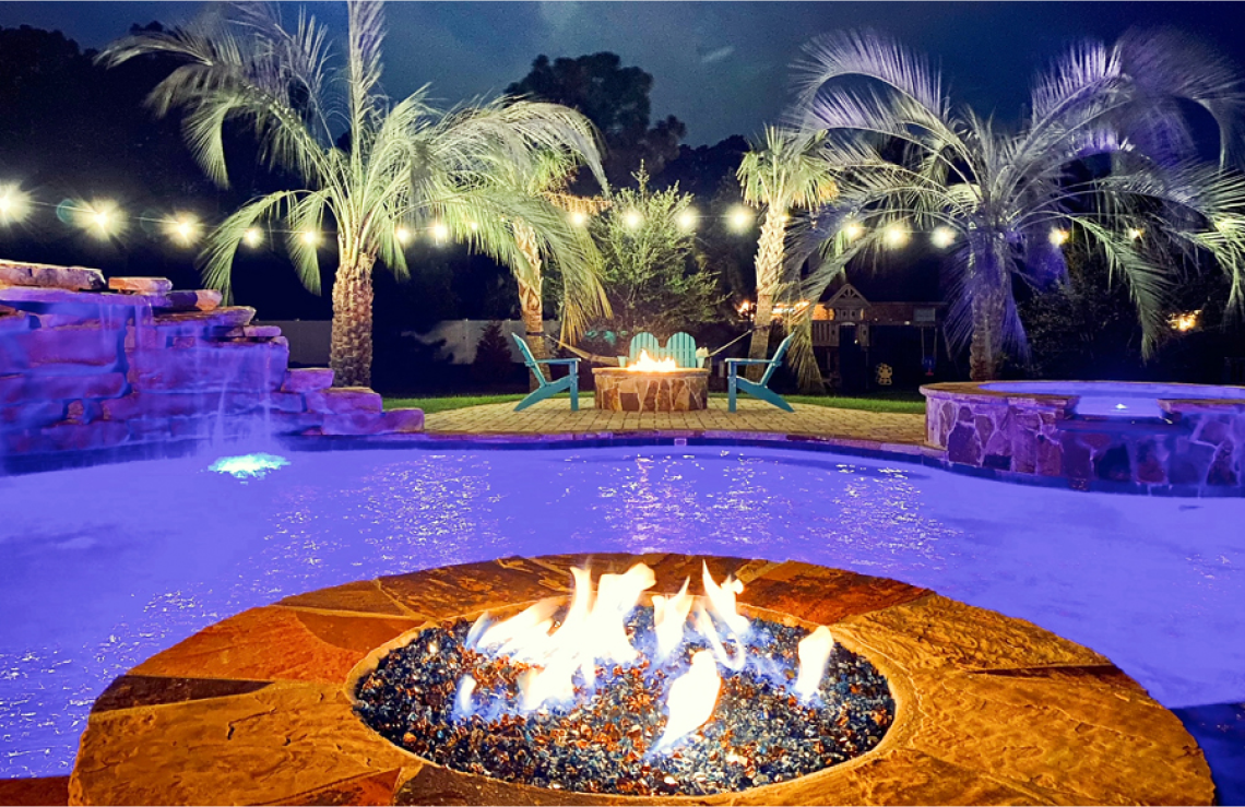 Fire pit adjacent to swimming pool illuminated in purple.