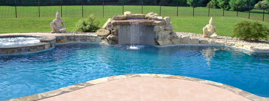 Rock grotto-style waterfall with decorative figurines on a swimming pool in a Connecticut backyard.
