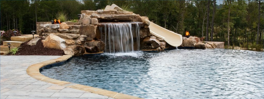 Large grotto waterfall with integrated slide on dark bottom swimming pool.
