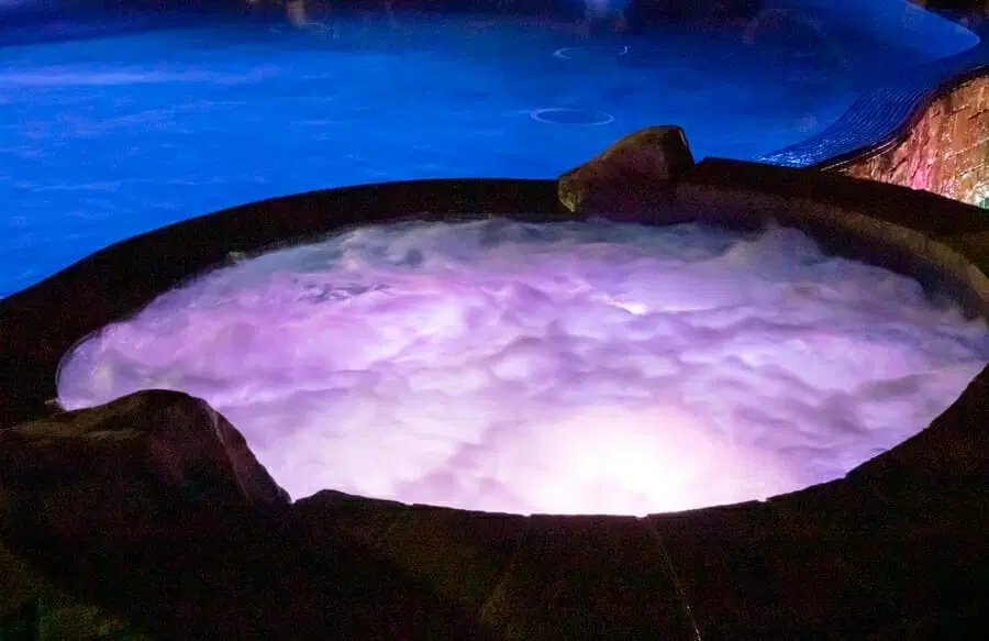 Swimming pool spa with water jets on illuminated with purple light at night.
