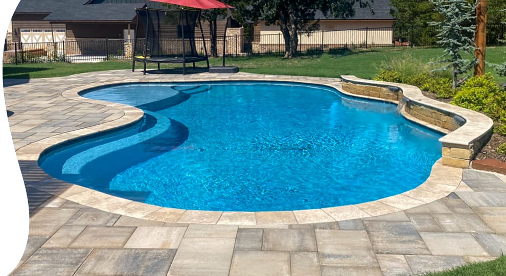 Curvy swimming pool with raised wall and cascade water features and paver decking.