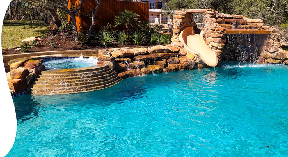 Rustic-style custom pool with spa, and rock grotto waterfall with integrated pool slide.