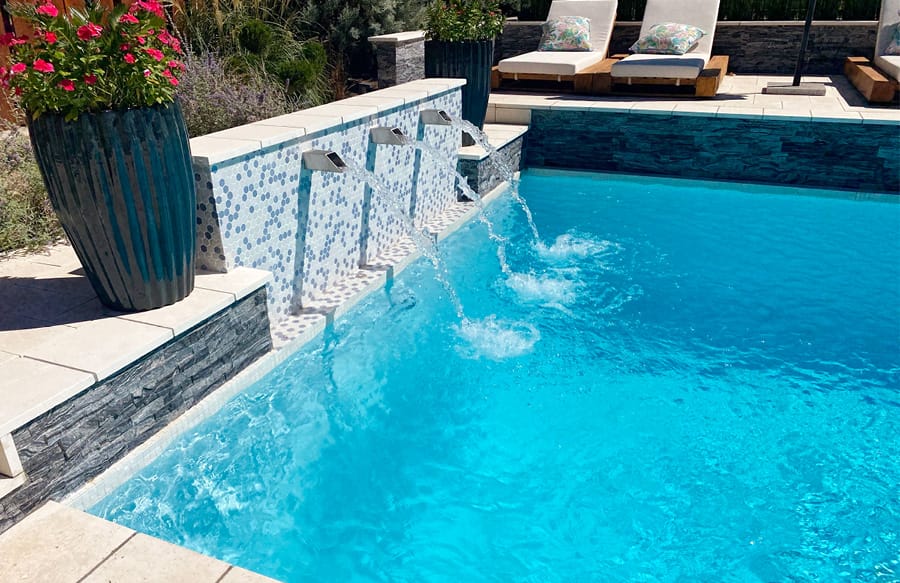 Sleek water feature installation with trio of metal spouts on a custom pool.