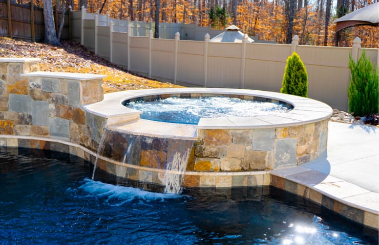 Round elevated spa with stone fascia on a swimming pool.