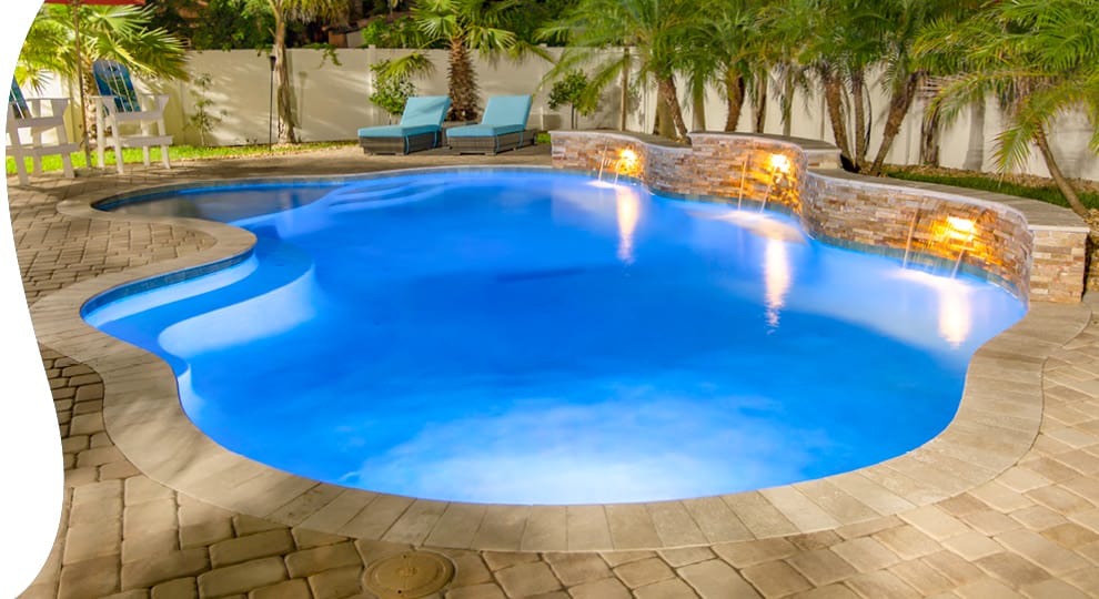 Cloud-shaped pool with cascade water features illuminated at night.