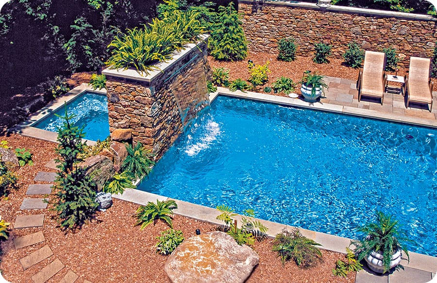 Inground swimming pool with decorative, stone-covered wall and custom planter separating it from the spa.