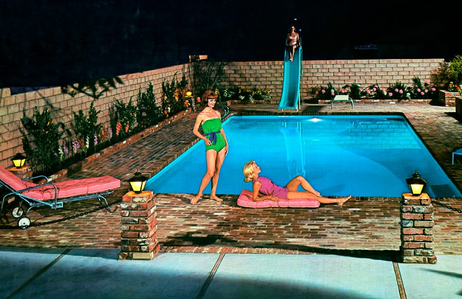 1960s-era women standing around a rectangular swimming pool at night.