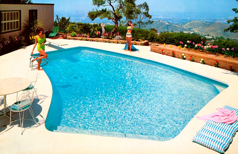 1960-era geometric shape swimming pool with two women in swimsuits standing on the deck.