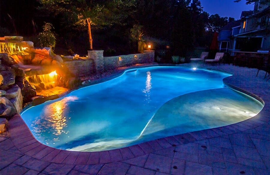 Inground pool at night in blue light with rock waterfall in golden light.