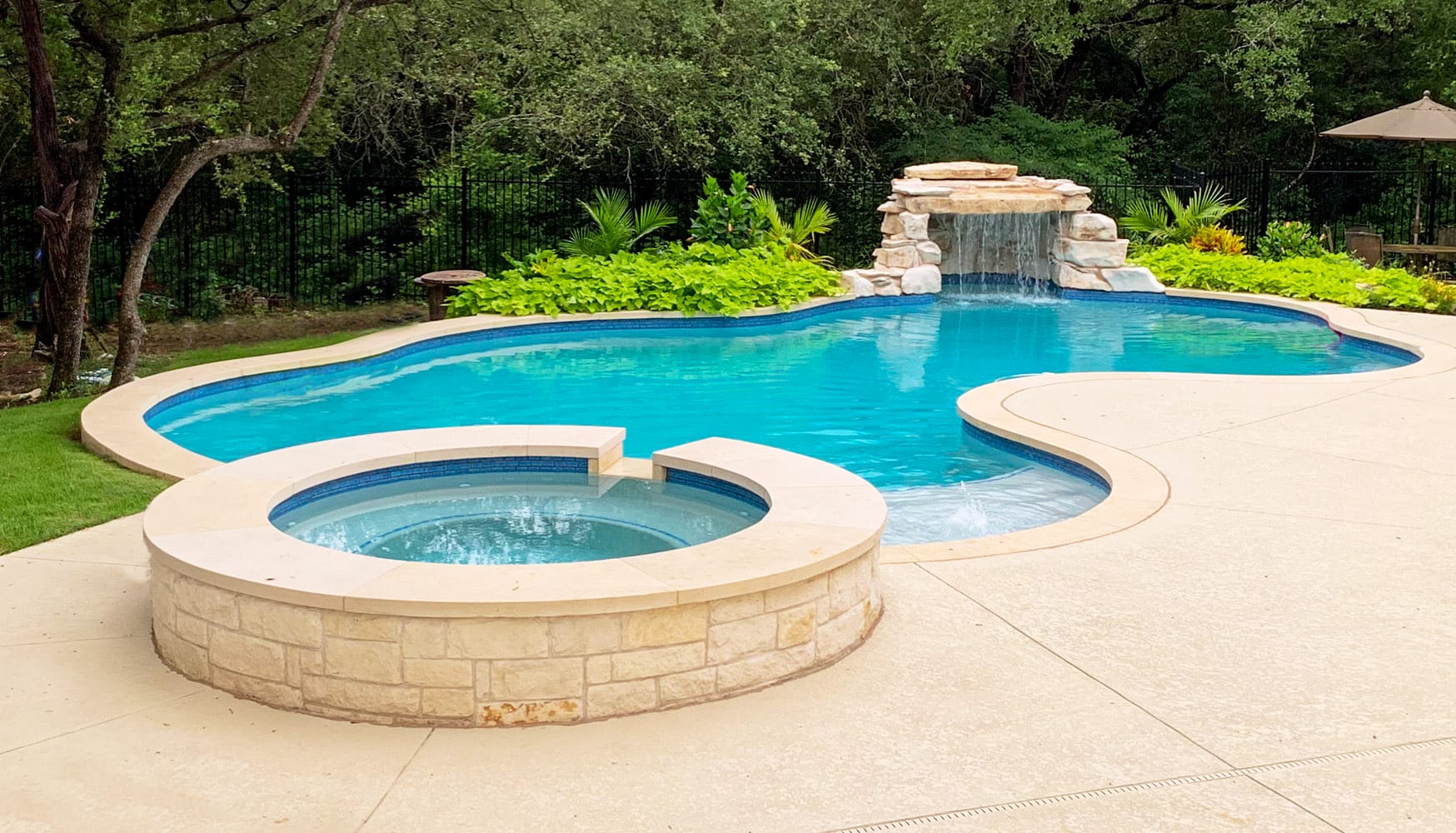 Curvy inground pool with waterfall and integrated landscape pocket.