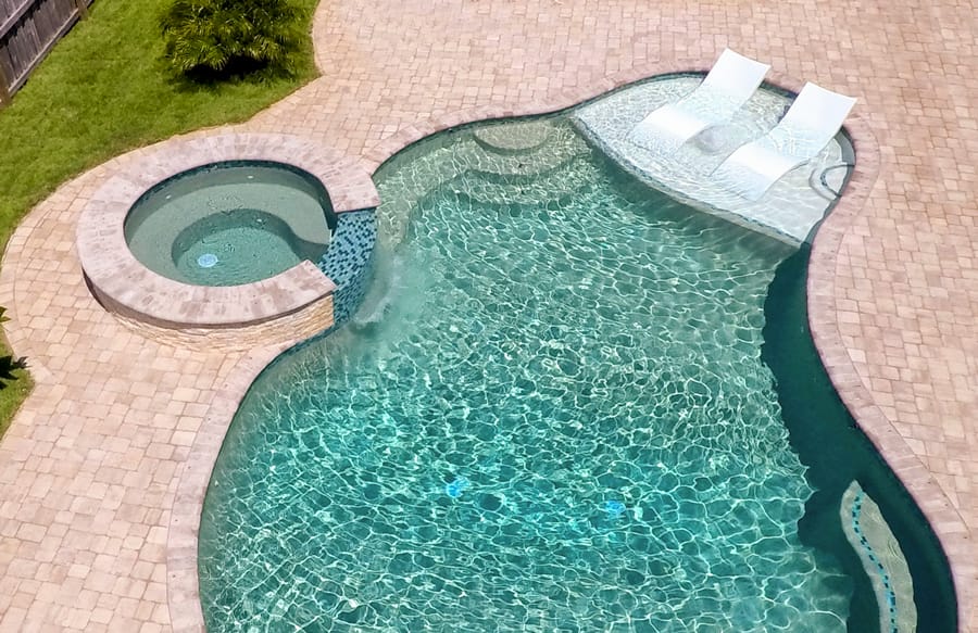 Curvy pool and spa wirh tanning shelf and sparkling teal water.