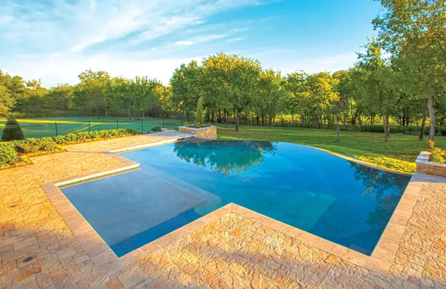 Infinity swimming pool in grassy, tree-filled backyard.