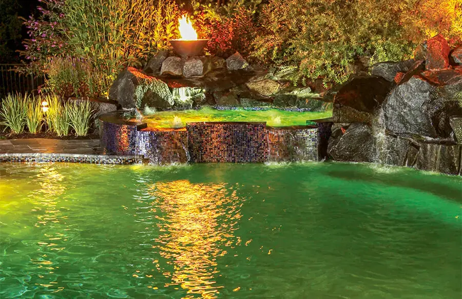 Custom spa on swimming pool at night with water illuminated in green light.