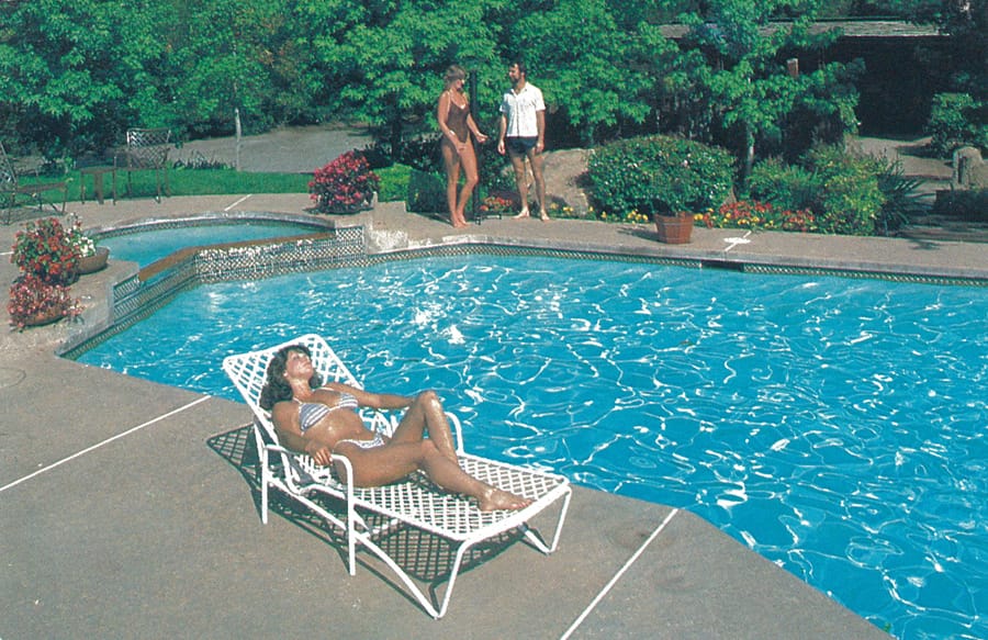 1980s woman is lounging in chaise by swimming pool.