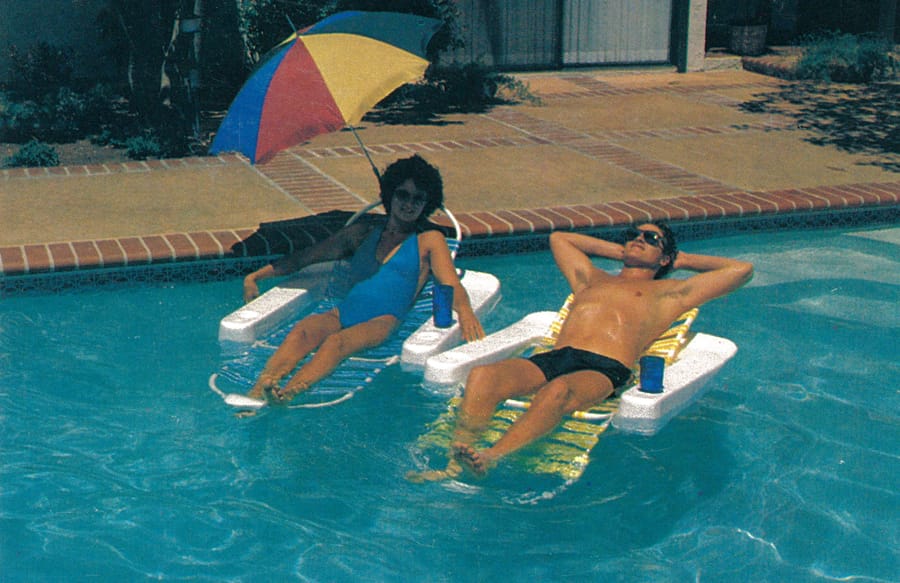 Early 1980s man and woman lounging on floats in swimming pool.