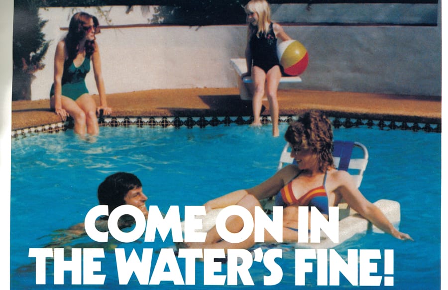 1980s-era girls sitting on edge of pool with two adults in the pool.
