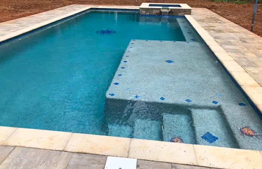 Tanning ledge with blue accent tile on rectangle inground pool.