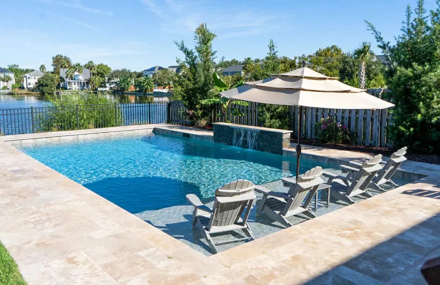 Rectangle swimming pool with sun shelf, four upright chairs, and patio umbrella.