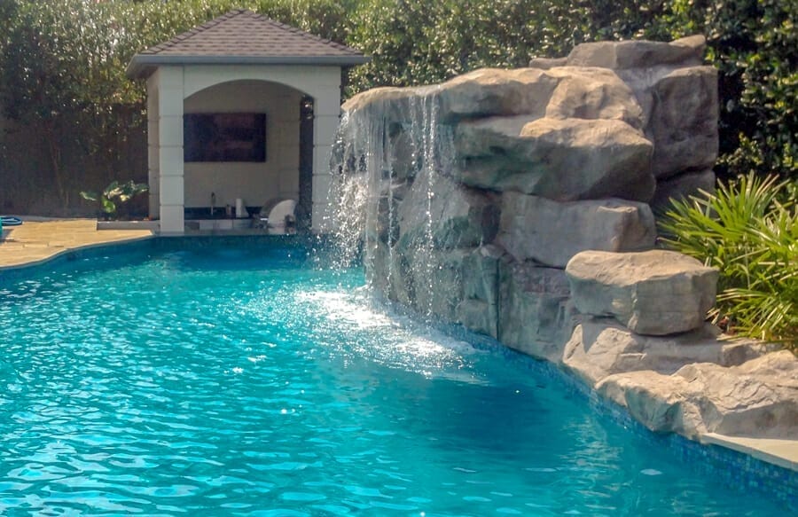 Rock waterfall on swimming pool with swim-up bar and outdoor kitchen.