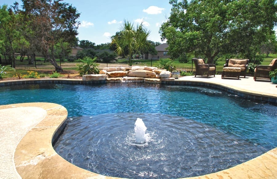 Free-form pool with bubbler fountain on tanning ledge.