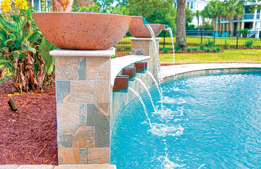 Two round concrete water bowls and three metal scupper fountains on raised wall of custom pool.