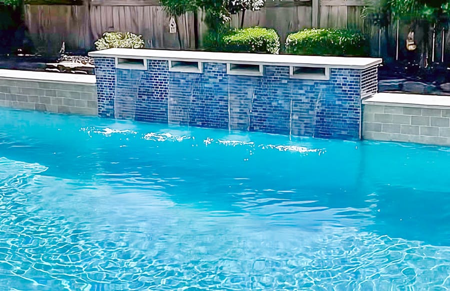 Inground pool with scupper waterfall installation and sparkling blue water.
