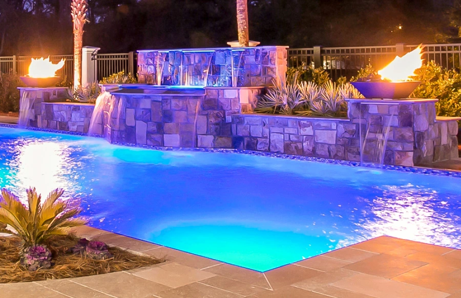 Inground pool with twin fire bowls and multiple cascade water features at night.