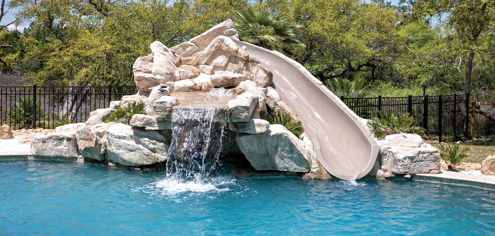 Grotto-style rock waterfall with integrated slide on swimming pool.