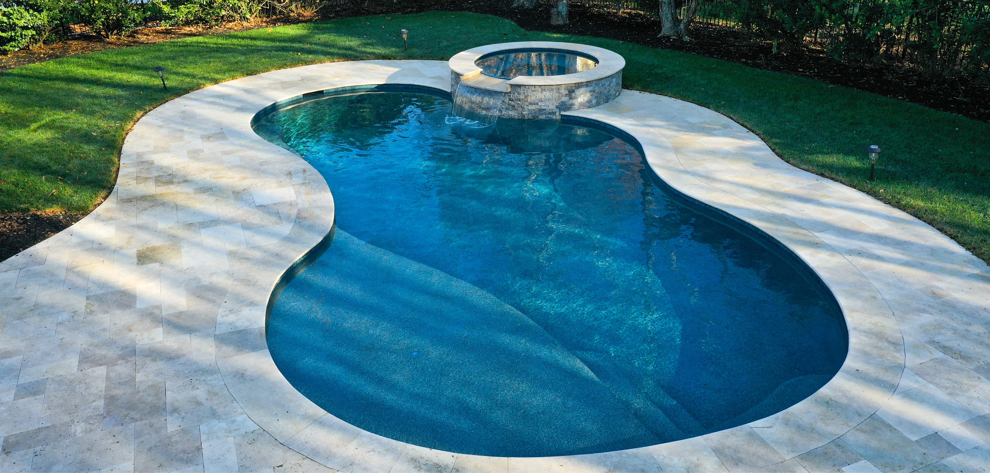 Figure-8 gunite pool with spa and stone deck in a lush backyard.