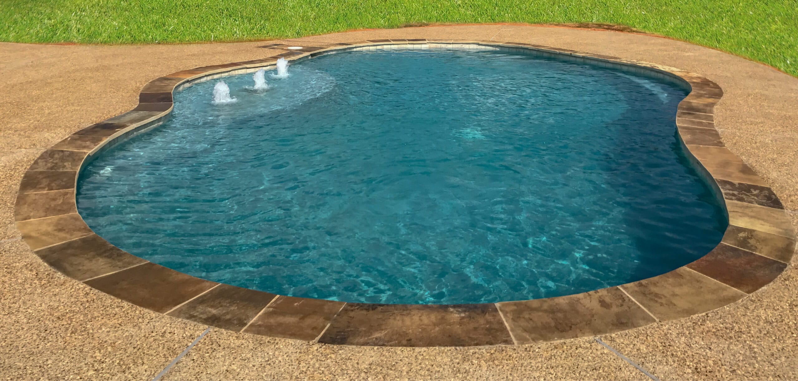Curvy inground pool with flagstone coping and three fountains on entry step.