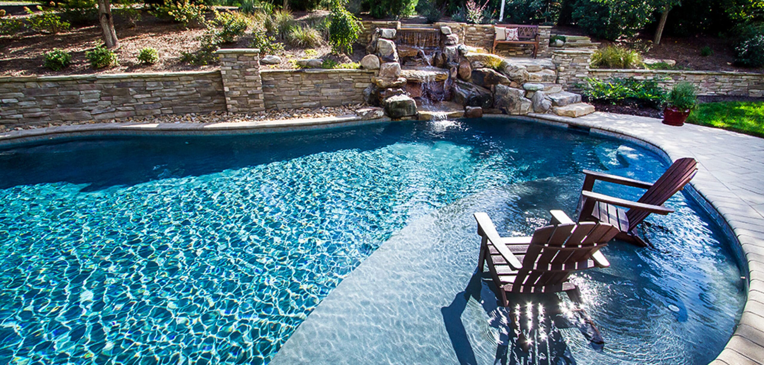 Custom pool with rock waterfall and lounge chairs on tanning shelf.