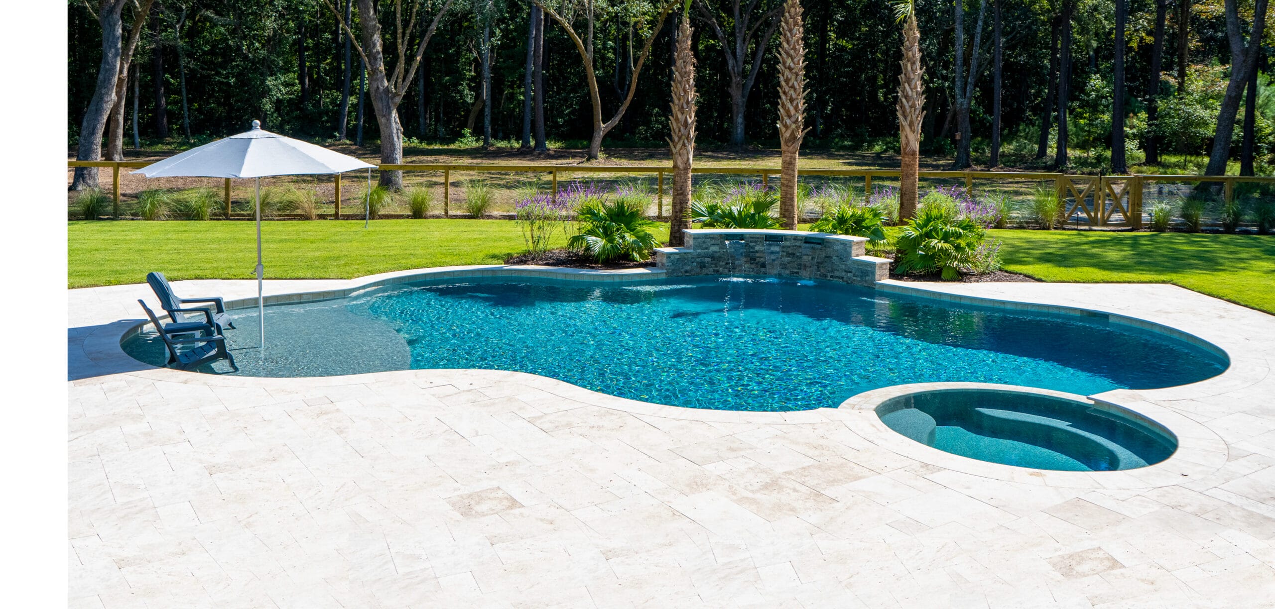 Curvy inground pool with spa, water features, and upright chairs and umbrella on its tanning shelf.